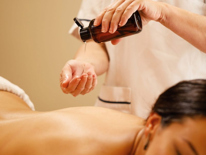 Unrecognizable therapist pouring oil in her hands before massage treatment at the wellness center,